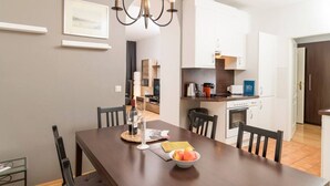 Een eetgedeelte met een houten tafel, stoelen, een kroonluchter en een schaal fruit.