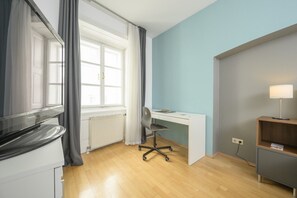 A room with a wooden floor, a white desk, a chair, a television, a radiator, and a lamp.