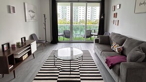 Ein modernes Wohnzimmer mit großem Fenster, einem runden Glastisch, einem grauen Sofa und einem Streifenmuster-Teppich.