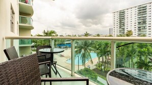 Ein Balkon mit Korbmöbeln, einem Pool und Blick auf ein Hochhaus.