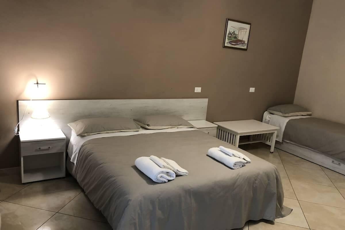 A hotel room with a large bed, a bedside table, a nightstand, and a small table with a chair.