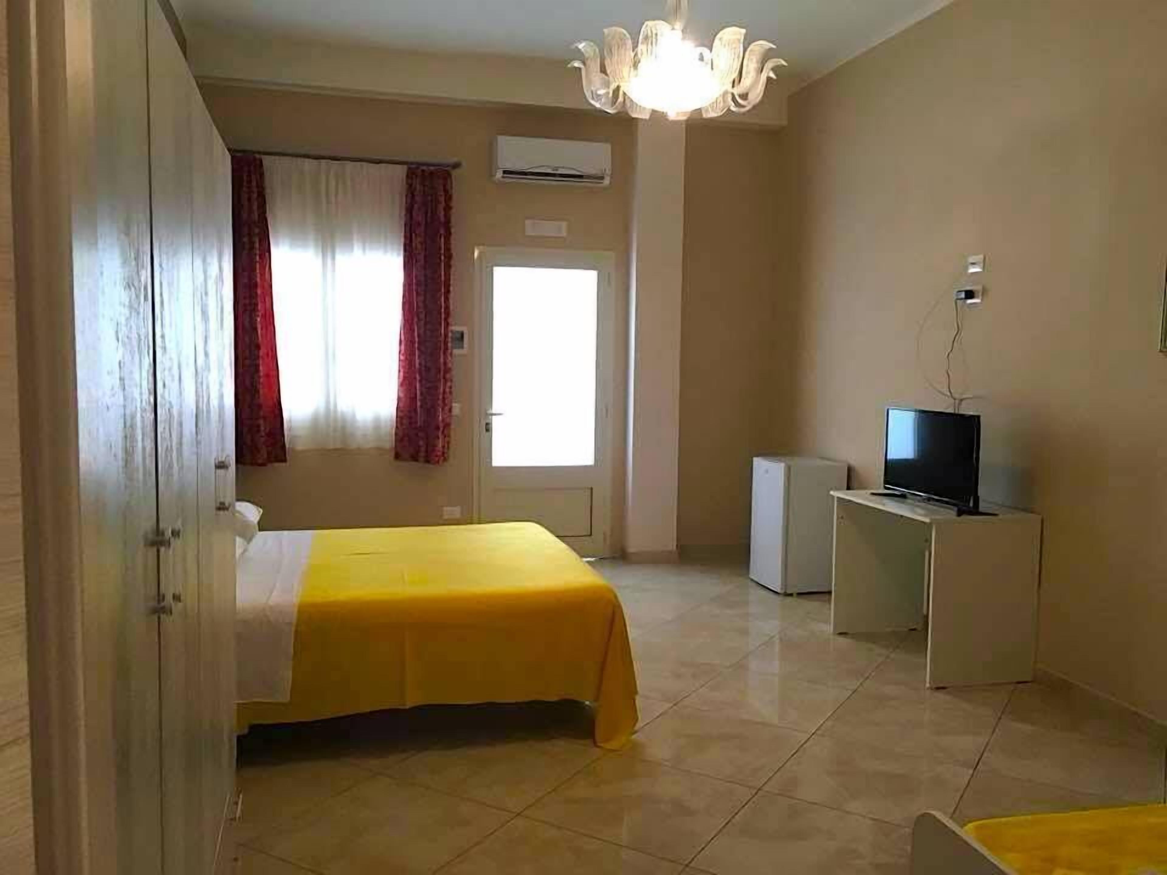 Una habitación de hotel con una cama, un televisor sobre un mueble, un equipo de aire acondicionado y una puerta con ventana.