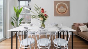 A modern dining area with a white table set for four, surrounded by white chairs. A vase with flowers is on the table, and a framed artwork is on the wall. - Rozelle Retreat by the Bay Run (Rozelle)