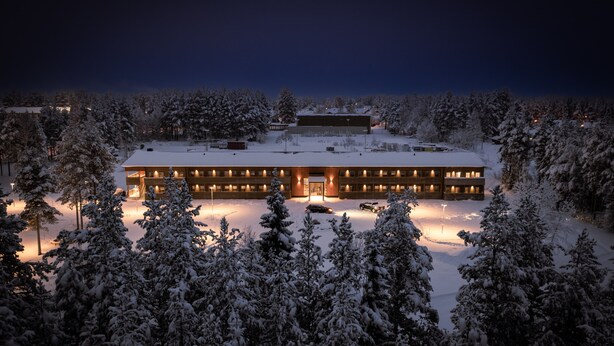 Un edificio grande de varios pisos con fachada simétrica, rodeado de árboles cubiertos de nieve.