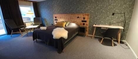 A modern hotel room with a large bed, a desk, and a chair.