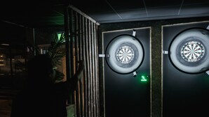 Una habitación con dos dardos fijos en la pared, un panel de madera y una señal de salida verde.