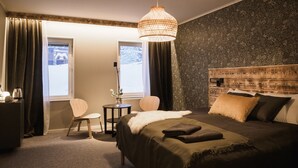 Una habitación de hotel con cama, escritorio, silla y ventana con cortinas.