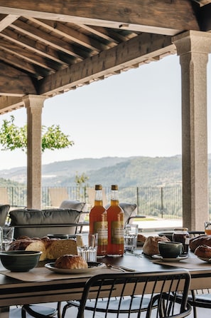 Un espace de restauration en plein air avec une table dressée pour deux personnes, comprenant du pain, une bouteille de vin et un verre.