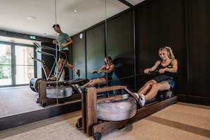 Une salle de sport équipée de rameurs et dotée d’un murmiroir.