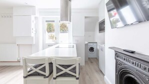 A modern kitchen with a central island, a washing machine, and a fireplace. - Sleek & Well-connected Studio Flat Archway! (London)