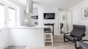 A modern kitchen with a central island, a built-in microwave, and a flat-screen TV. - Sleek & Well-connected Studio Flat Archway! (London)