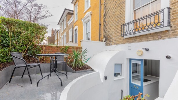 A courtyard with a table and chairs, a blue door labeled '22A', and a white wall with a small window. - Sleek & Well-connected Studio Flat Archway! (London)