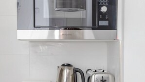 A compact kitchen with a stainless steel microwave, a Russell Hobbs electric kettle, and a toaster on a white countertop. - Sleek & Well-connected Studio Flat Archway! (London)
