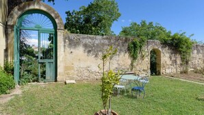 A rustic stone wall with a green archway and a small table with chairs in a grassy area. - Château Teillan - Cadran Solaire (Aimargues)