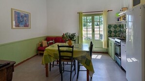 A dining area with a table and chairs, a sofa, a window with curtains, and a kitchen with appliances. - Château Teillan - Cadran Solaire (Aimargues)