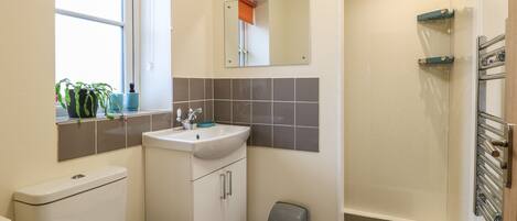 A compact bathroom with a toilet, sink, mirror, and shower.