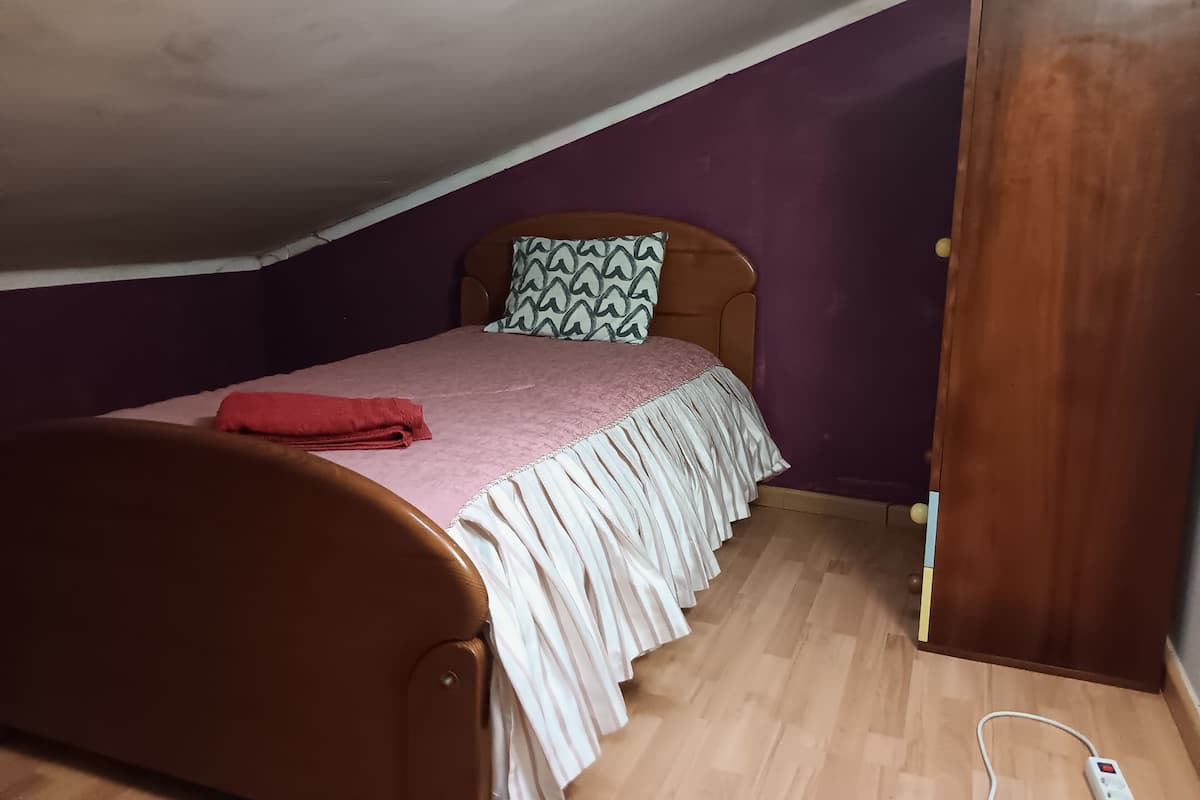 Une chambre avec un lit en bois, des murs violets, une armoire en bois et un plancher en bois.