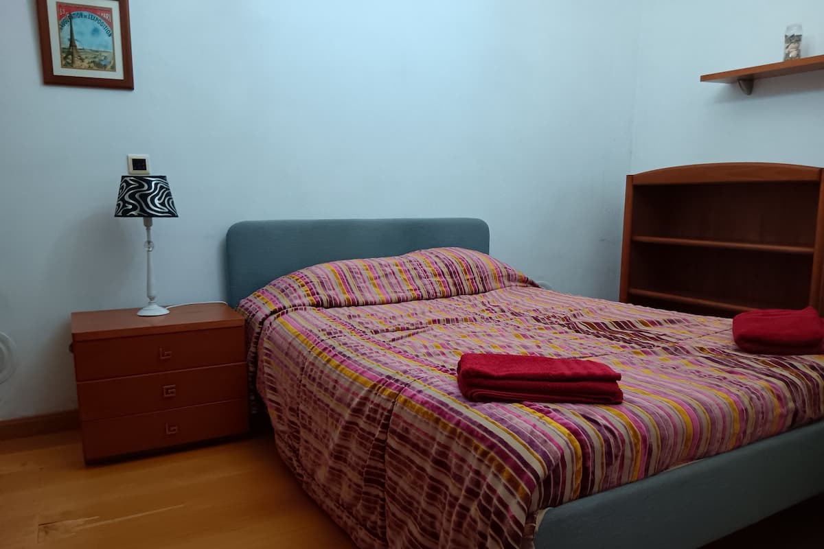 Une chambre à coucher avec un lit, une table de chevet, une lampe, une commode et une étagère.