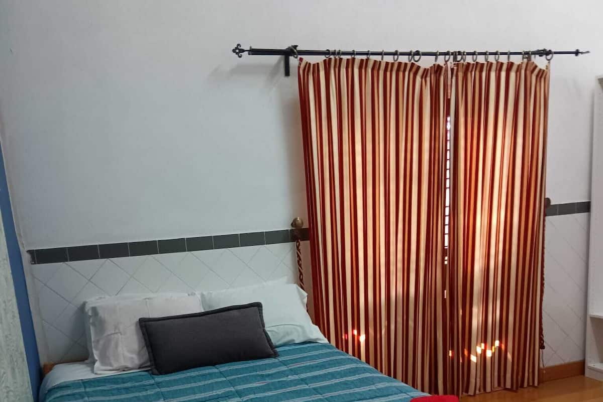 Un lit avec une couvre-lit bleue et turquoise à rayures, deux serviettes rouges et un rideau à rayures.