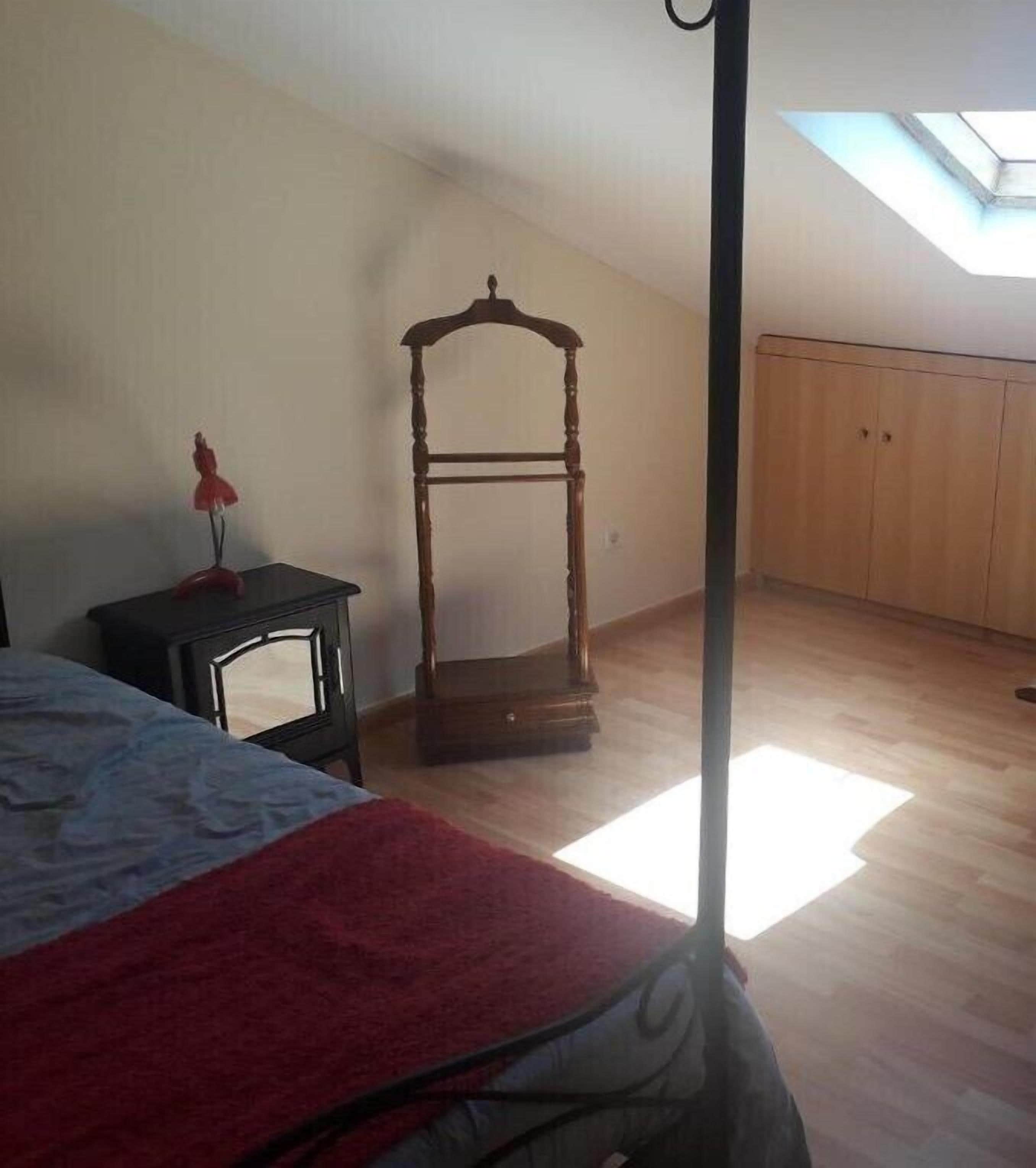Un dormitorio con una cama, un armario de madera, una mesita de noche con una lámpara y un tragaluz.