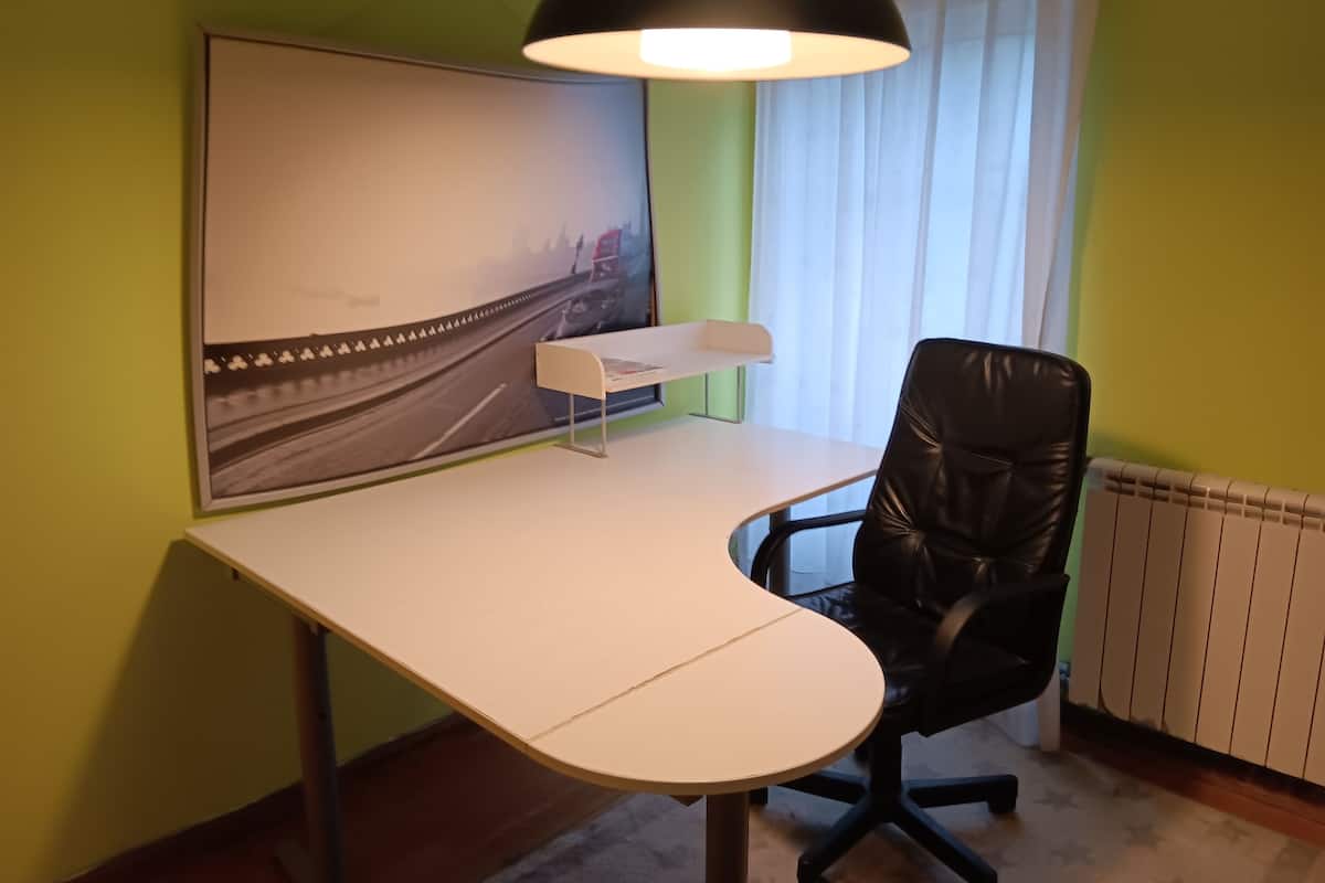 Un espace de bureau moderne avec un bureau incurvé, un fauteuil en cuir noir, une lampe de bureau blanche et un grand tableau encadré accroché au mur.