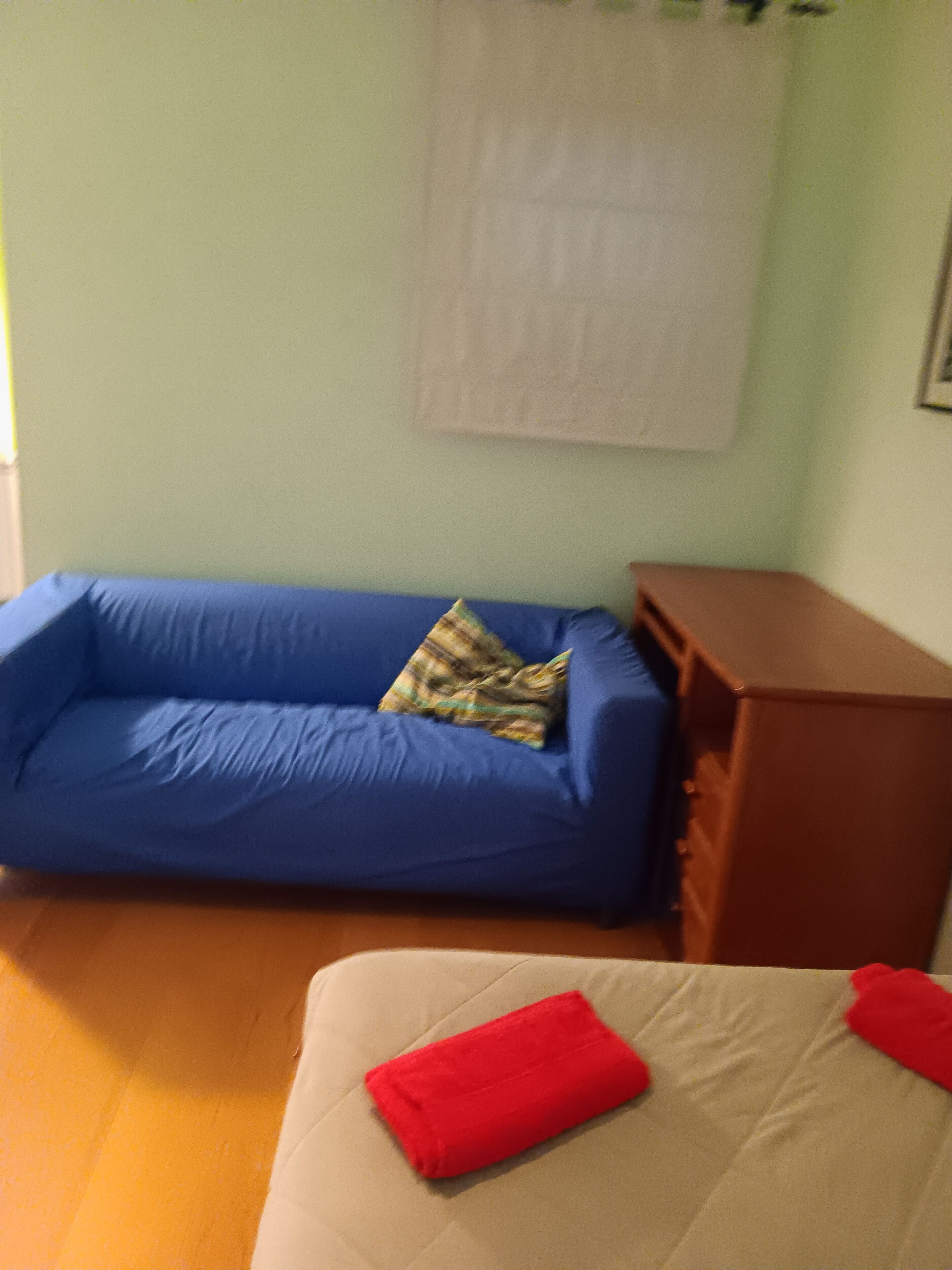 Una habitación con un sofá azul, un armario de madera y una cama con una almohada roja.