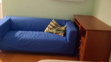 Una habitación con un sofá azul, un armario de madera y una cama con una almohada roja.