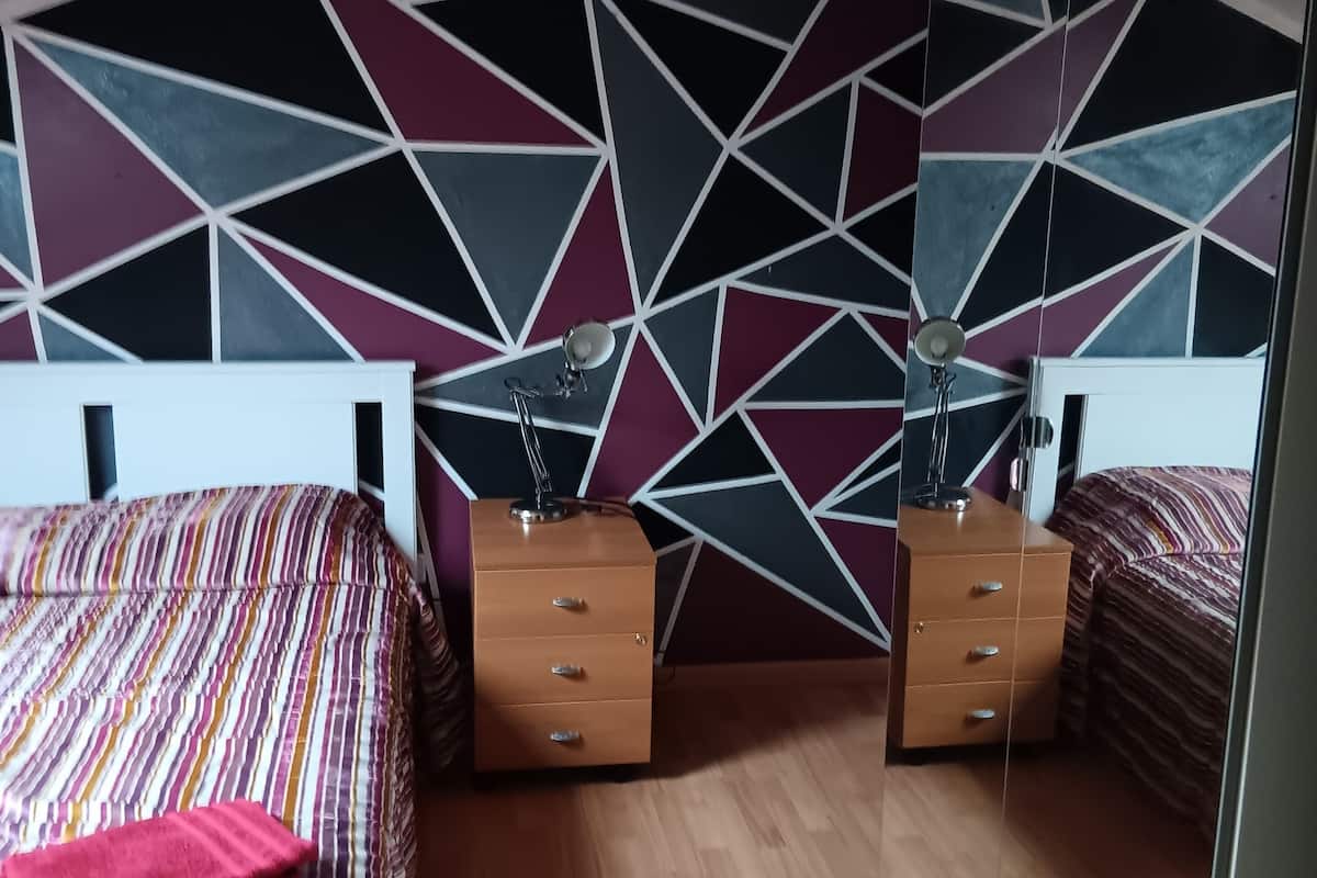 Une chambre avec deux lits, des tables de chevet en bois, un mur orné d’un motif géométrique et un plafond en pente.