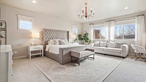 A bedroom with a large bed, a bedside table, a chair, a desk, and a window. - Large Modern 5 Bedroom Custom Home (Meridian)