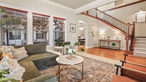 A spacious living room with a green sofa, a round coffee table, and a staircase leading to an upper level. - Large Modern 5 Bedroom Custom Home (Meridian)