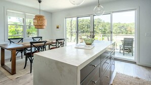 Une cuisine moderne dotée d’un grand îlot central, d’un coin repas et de grandes fenêtres offrant une vue sur l’extérieur.