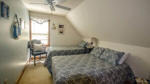 Ein Schlafzimmer mit zwei Betten, einem Deckenventilator, einem Fenster mit Vorhängen und einem Sessel.