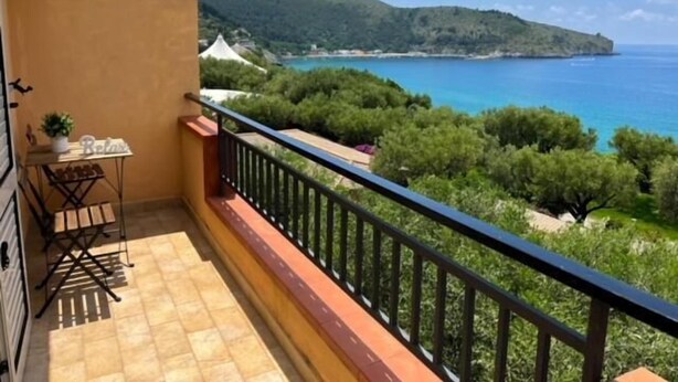 A balcony with a view of a coastal landscape, including trees and a body of water.
