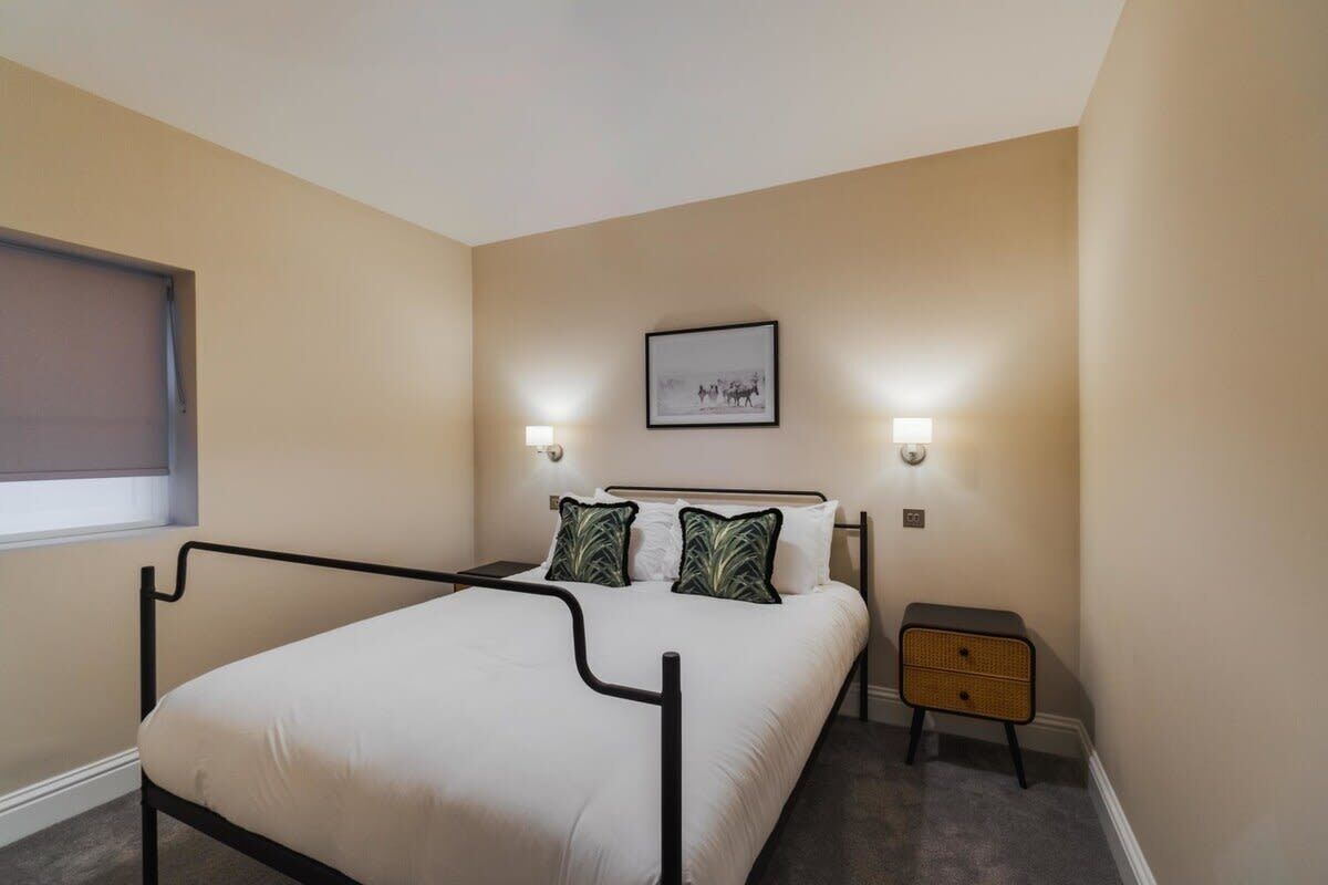 A bedroom with a bed, bedside lamps, a nightstand, a window, and a framed picture on the wall.