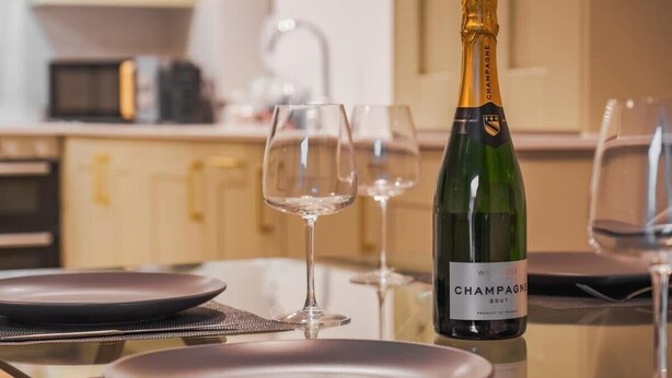 A dining table with a bottle of champagne, glasses, and plates. - Modern 2 Bed Ground Floor - Parking - By Tempstay (Berkshire)