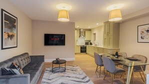 A modern living room with a sofa, a TV, a dining table with chairs, and a kitchen in the background. - Modern 2 Bed Ground Floor - Parking - By Tempstay (Berkshire)