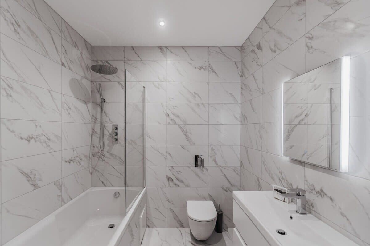 Un bagno moderno con vasca, servizi igienici e cabina doccia, caratterizzato da piastrelle in marmo e un grande specchio.