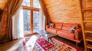 L’intérieur chaleureux d’un chalet, avec un décor en bois, un canapé, une table basse et une grande fenêtre agrémentée de rideaux.