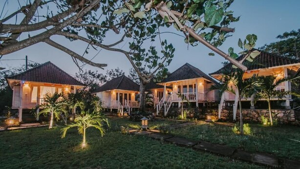 A row of houses with a well-maintained lawn and palm trees. - Paluh Beach Huts (Lembongan Island)