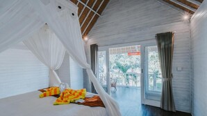 A bedroom with a bed, white curtains, and a view of the outdoors. - Paluh Beach Huts (Lembongan Island)