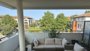 A balcony with wicker furniture, including a sofa and a small table, and a potted plant.