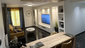 A modern living room with a sofa, a dining table, a TV, and a decorative wall piece.
