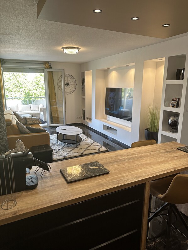 Ein modernes Wohnzimmer mit einer Holztrenne, einem Fernseher und einer Sitzecke mit Sofa und Sesseln.