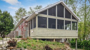 A two-story house with large windows and a sloped roof, surrounded by a landscaped garden with rocks and plants. - Leland Lodge: Downtown New Buffalo, Sleeps 14, Walk to Beach, 2 Jacuzzi Suites (New Buffalo)