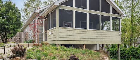 A two-story house with large windows and a sloped roof, surrounded by a landscaped garden with rocks and plants.