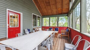A covered porch with a long table and chairs, wooden benches, and a red door. - Leland Lodge: Downtown New Buffalo, Sleeps 14, Walk to Beach, 2 Jacuzzi Suites (New Buffalo)