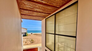 Una habitación con un gran ventanal que da a una playa, una puerta de madera y un techo de bambú.