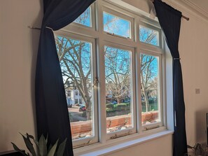 A room with a large window, curtains, and a potted plant. - Stylish 2 Bedroom Flat in the Heart of Barnes (London)