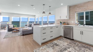 A modern kitchen with white cabinets, a built-in oven, and a view of the sea.