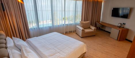 A hotel room with a large bed, a sofa, a desk, and a TV.